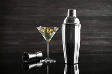 Photo of Metal shaker, Martini cocktail and jigger on black mirror surface