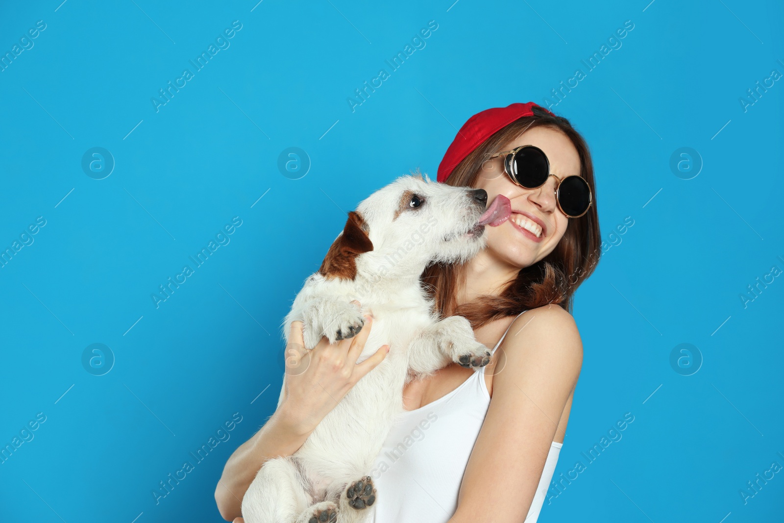 Photo of Young woman with her cute Jack Russell Terrier on light blue background. Lovely pet