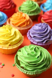 Photo of Delicious bright cupcakes and sprinkles on coral background, closeup