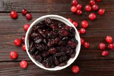 Tasty dried cranberries in bowl and fresh ones on wooden table, top view