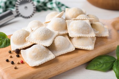 Uncooked ravioli, peppercorns and basil on white wooden table, closeup