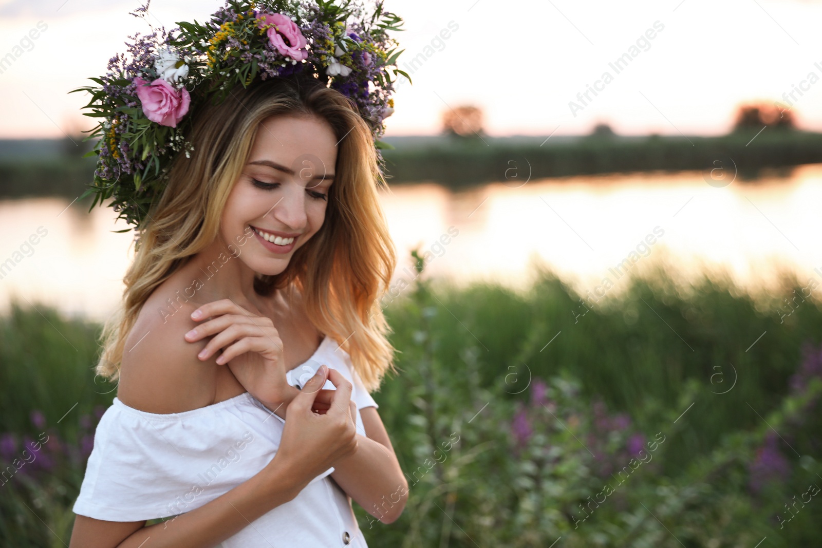 Photo of Young woman wearing wreath made of beautiful flowers outdoors at sunset