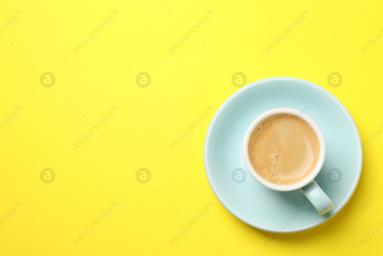 Photo of Aromatic coffee in cup on yellow background, top view. Space for text