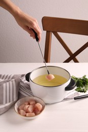 Photo of Woman dipping piece of raw meat into oil in fondue pot at white wooden table, closeup