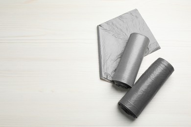Photo of Rolls of grey garbage bags on white wooden table, flat lay. Space for text