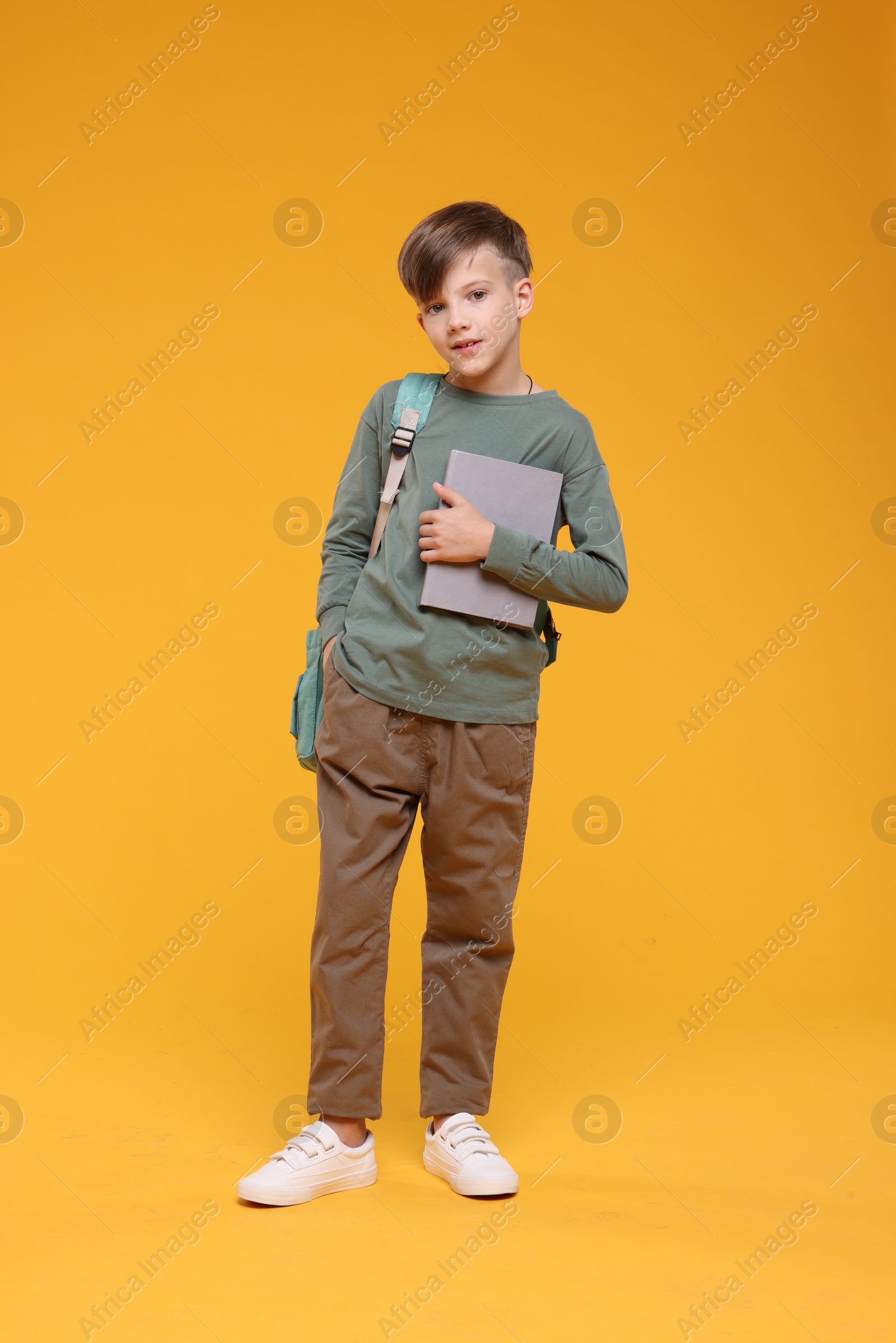 Photo of Cute schoolboy with book on orange background