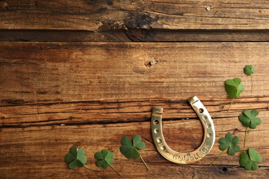 Photo of Clover leaves and horseshoe on wooden table, flat lay with space for text. St. Patrick's Day celebration