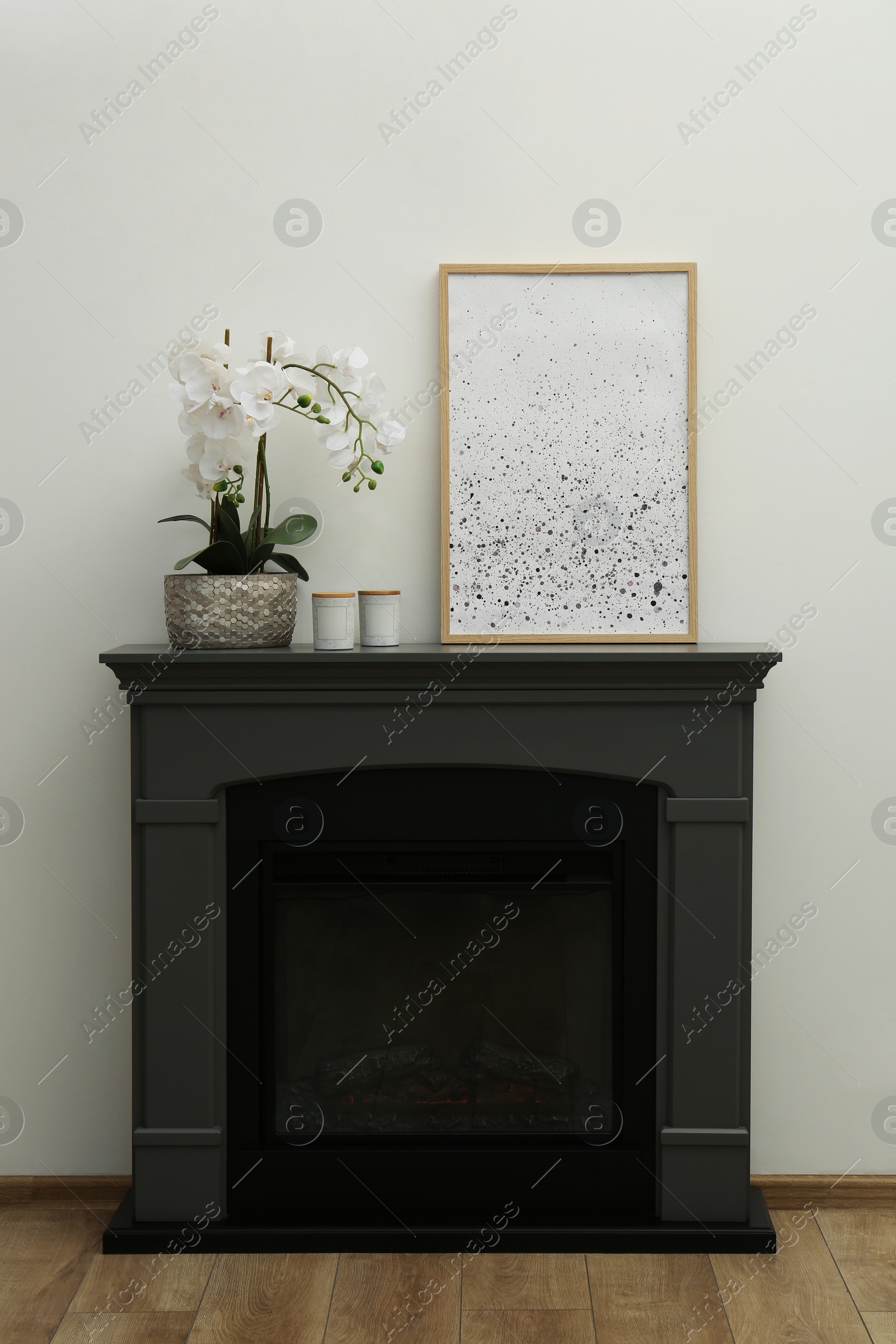 Photo of Picture frame, candles and orchid on fireplace near white wall indoors. Interior design