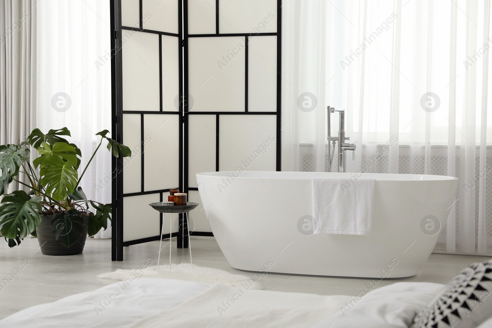 Photo of Stylish light apartment interior with white bathtub and bed