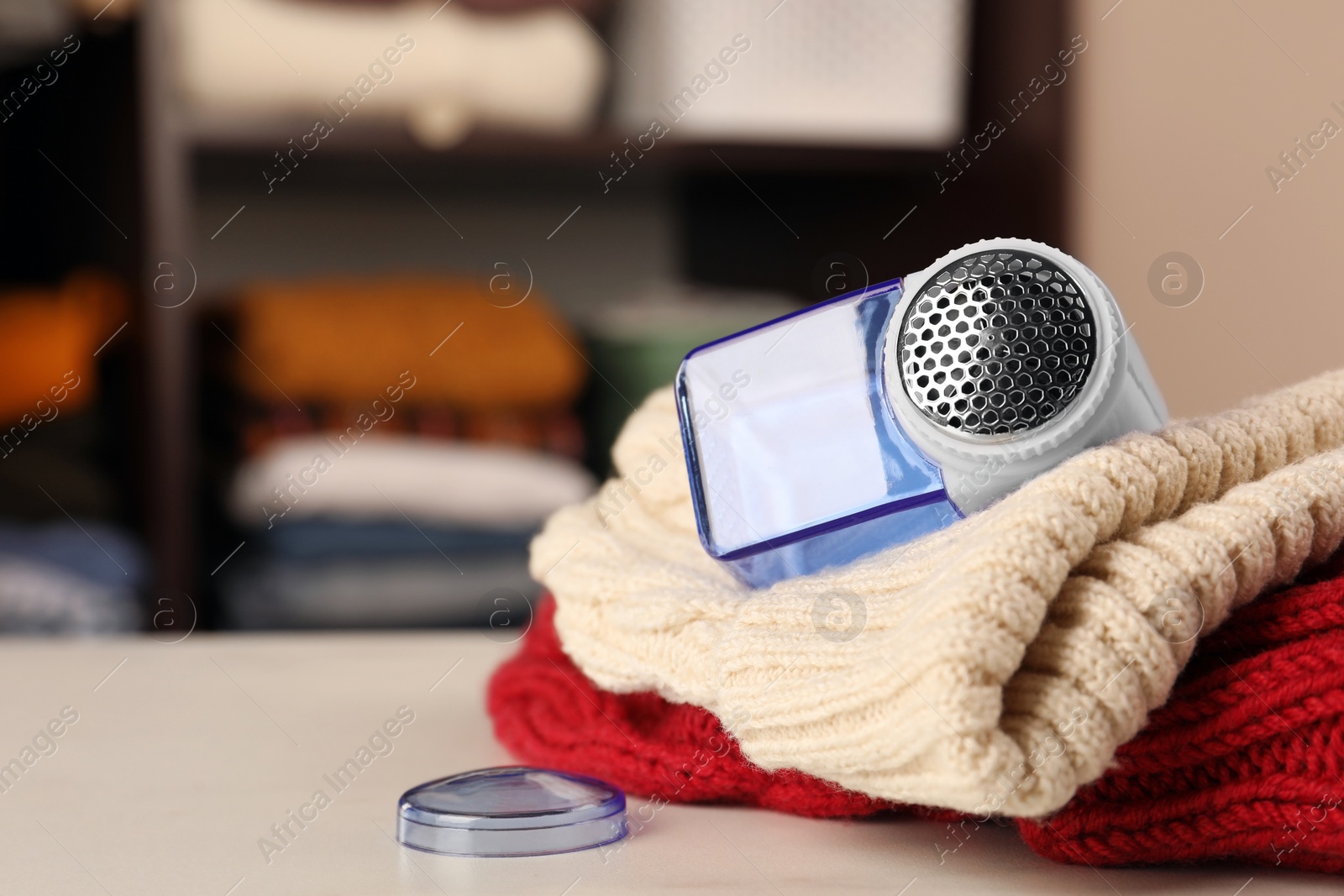Photo of Modern fabric shaver and knitted clothes on white table indoors, closeup. Space for text