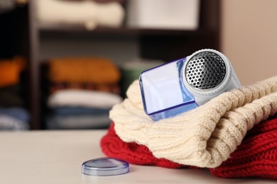 Photo of Modern fabric shaver and knitted clothes on white table indoors, closeup. Space for text