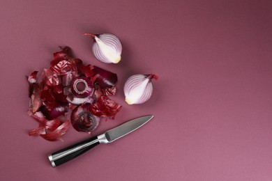 Photo of Cut red onions with peels and knife on dark pink background, flat lay. Space for text