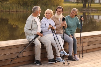 Photo of Group of senior people with Nordic walking poles sitting on wooden parapet outdoors