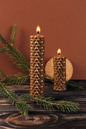 Photo of Stylish burning beeswax candles with spruce branches on wooden table