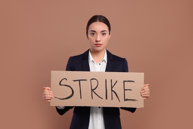 Photo of Young woman holding cardboard banner with word Strike on brown background