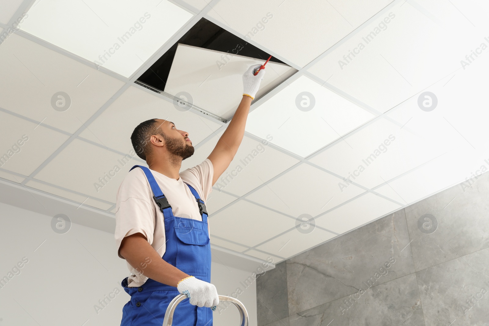 Photo of Electrician with screwdriver repairing ceiling light indoors, low angle view. Space for text