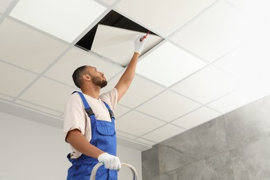 Electrician with screwdriver repairing ceiling light indoors, low angle view. Space for text