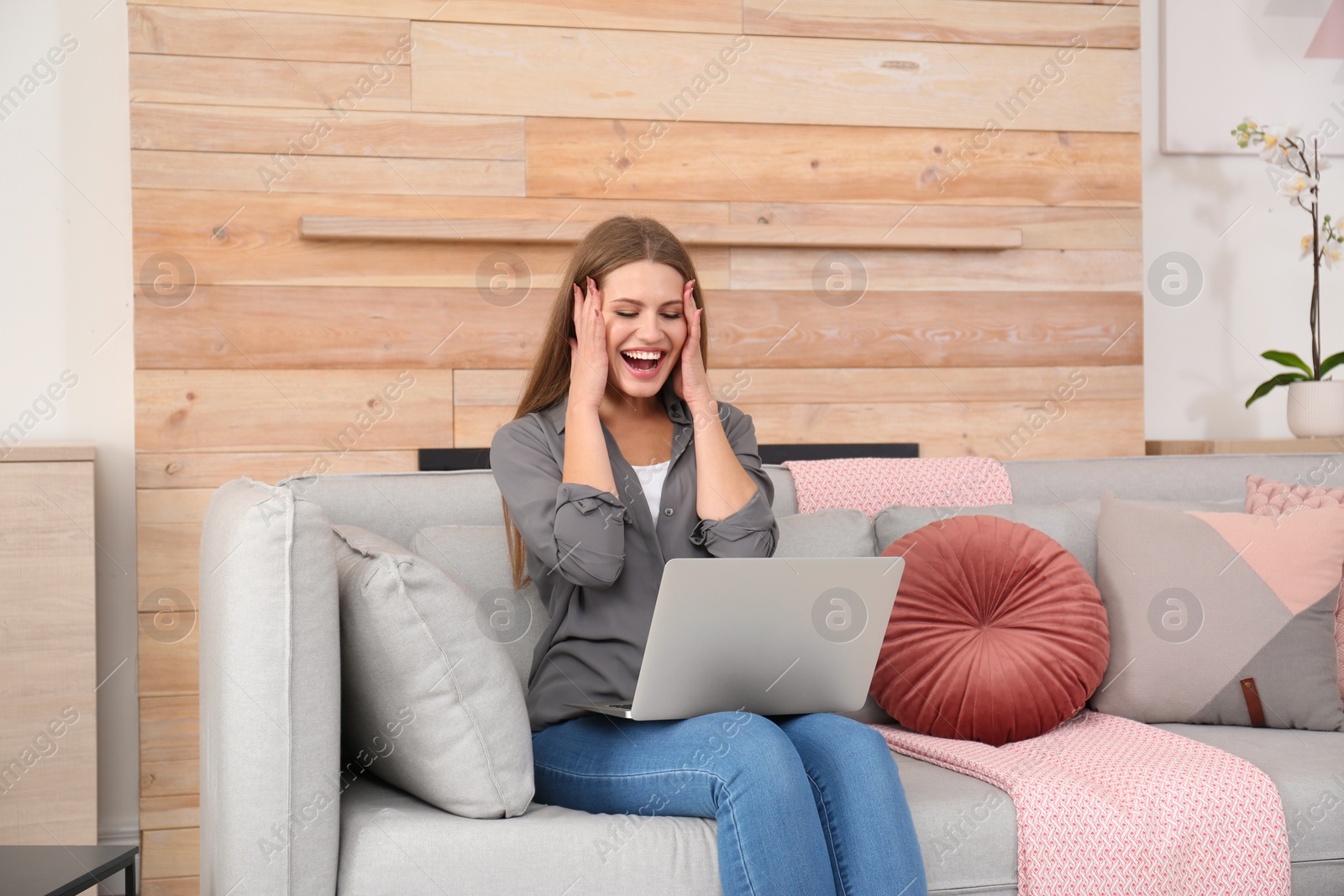 Photo of Emotional young woman with laptop celebrating victory on sofa at home