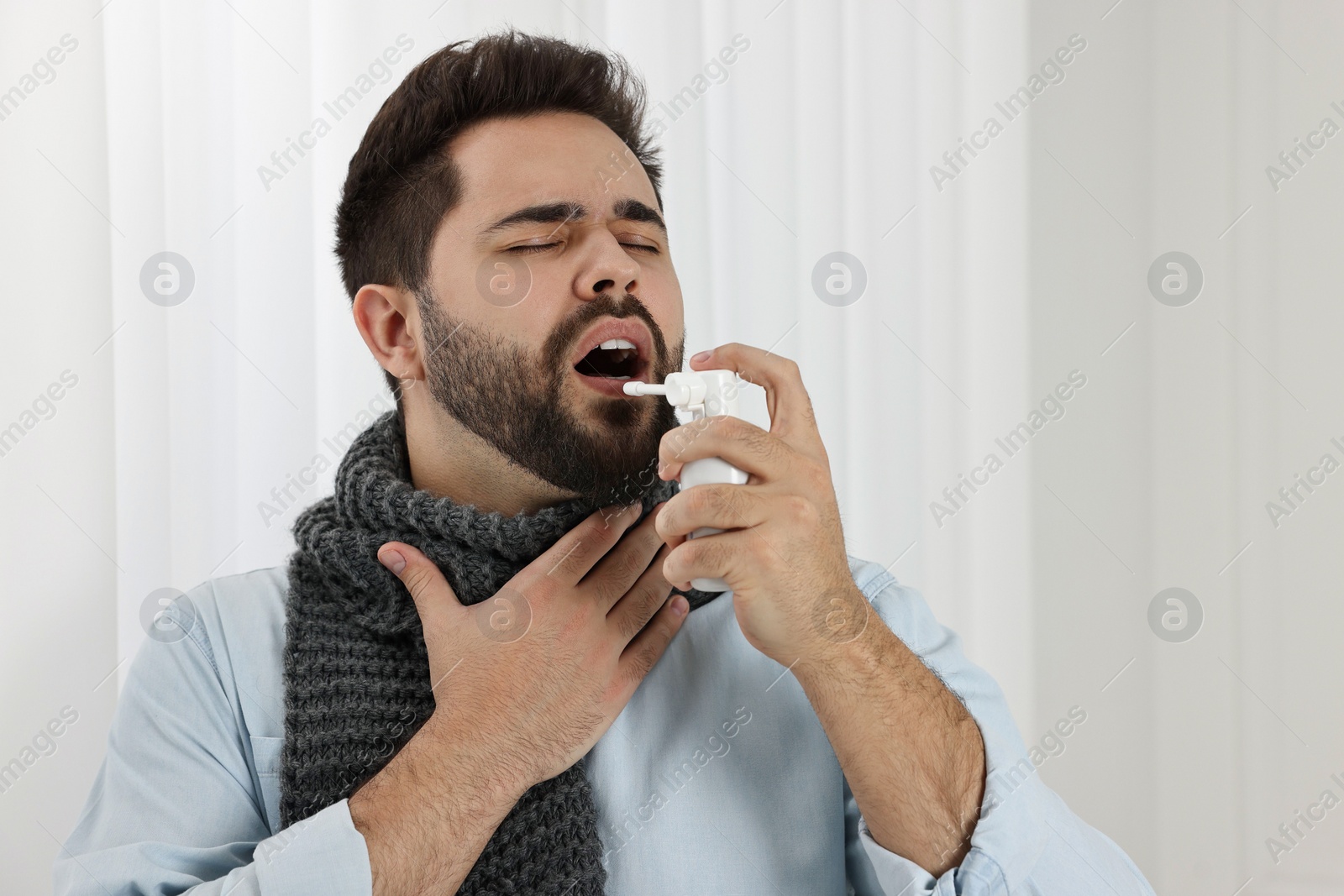 Photo of Young man with scarf using throat spray indoors