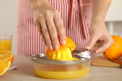 Photo of Woman squeezing orange juice at wooden table, closeup