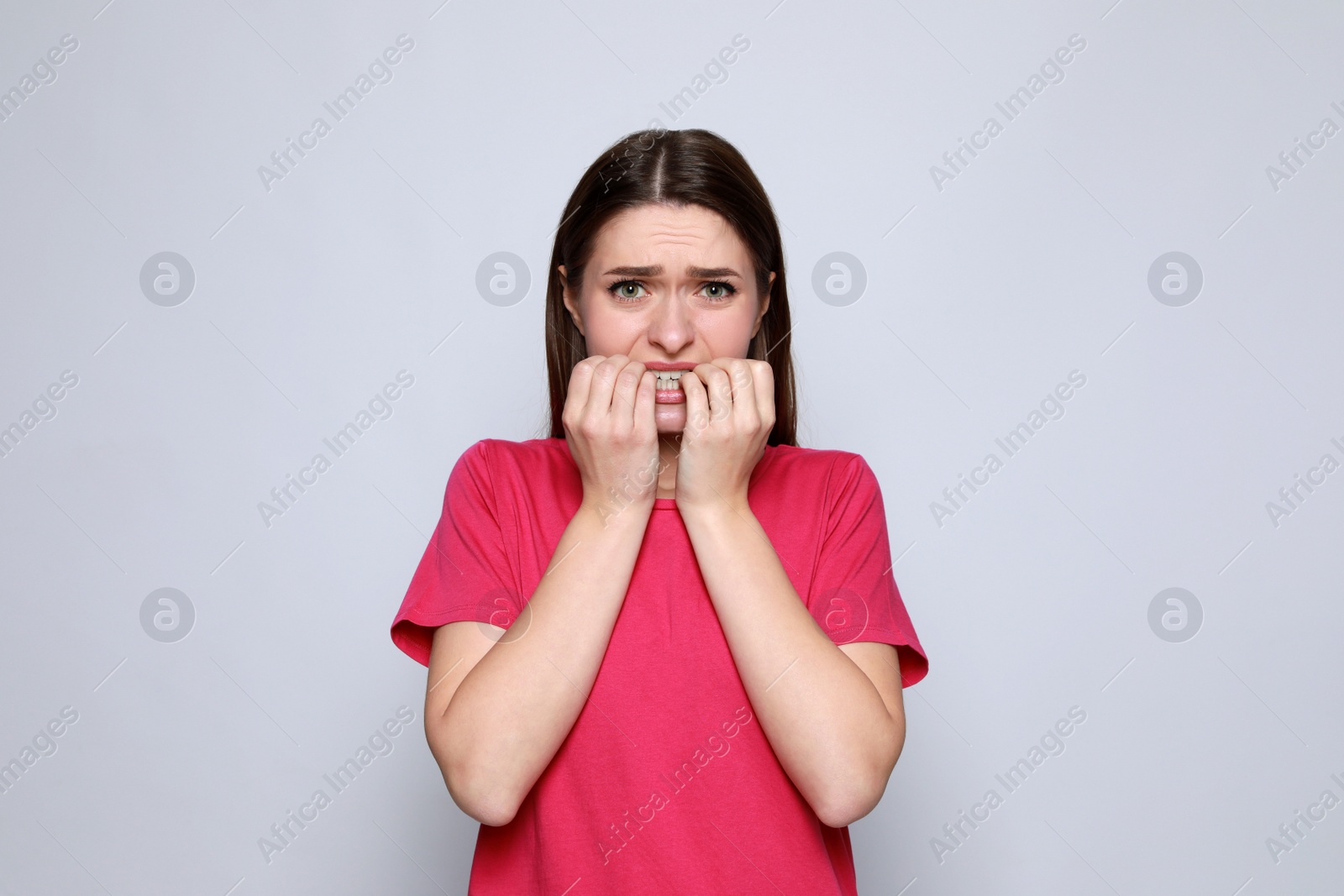 Photo of Young woman biting her nails on light grey background