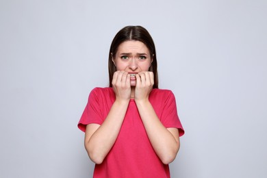 Photo of Young woman biting her nails on light grey background