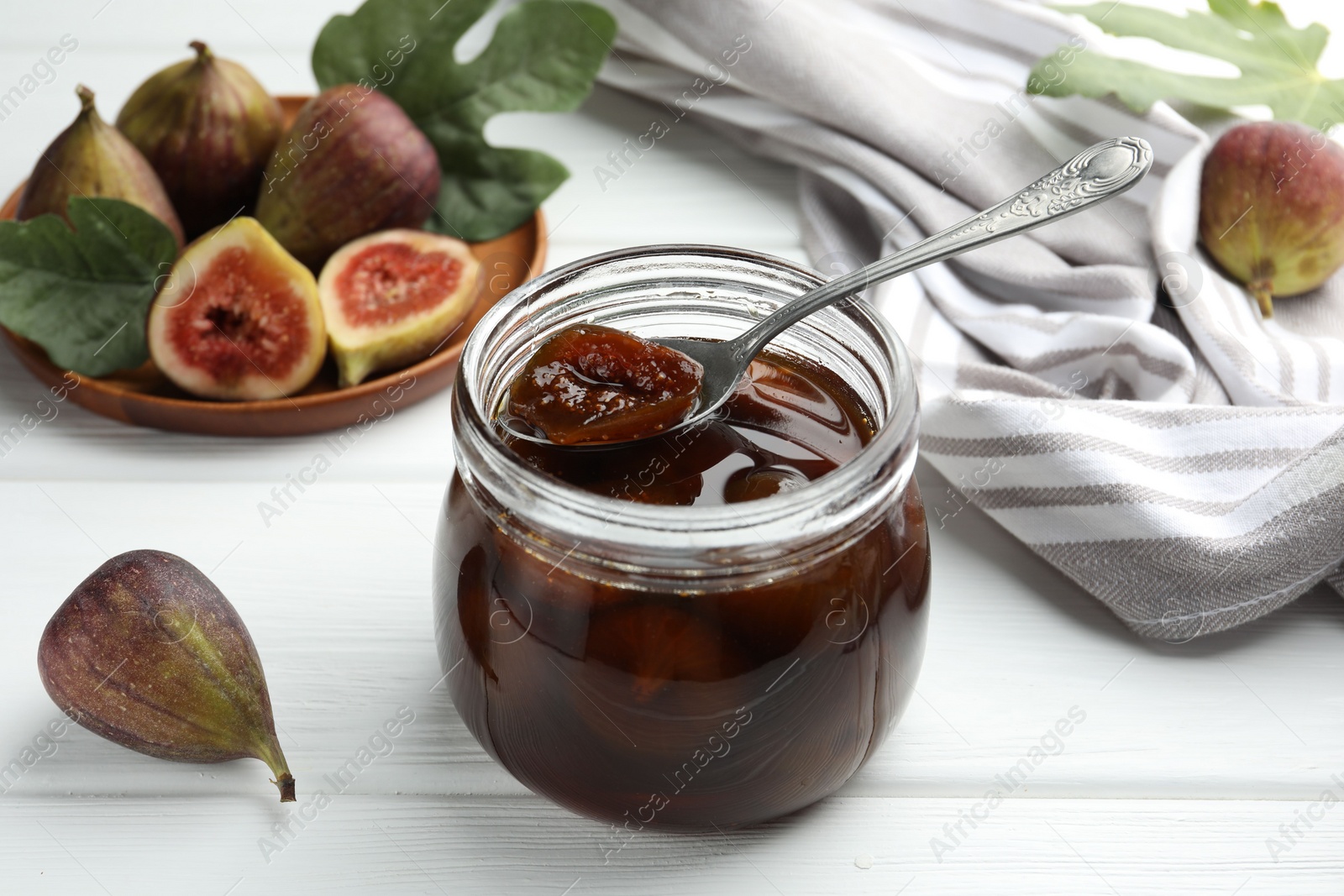 Photo of Jar of tasty sweet jam and fresh figs on white wooden table