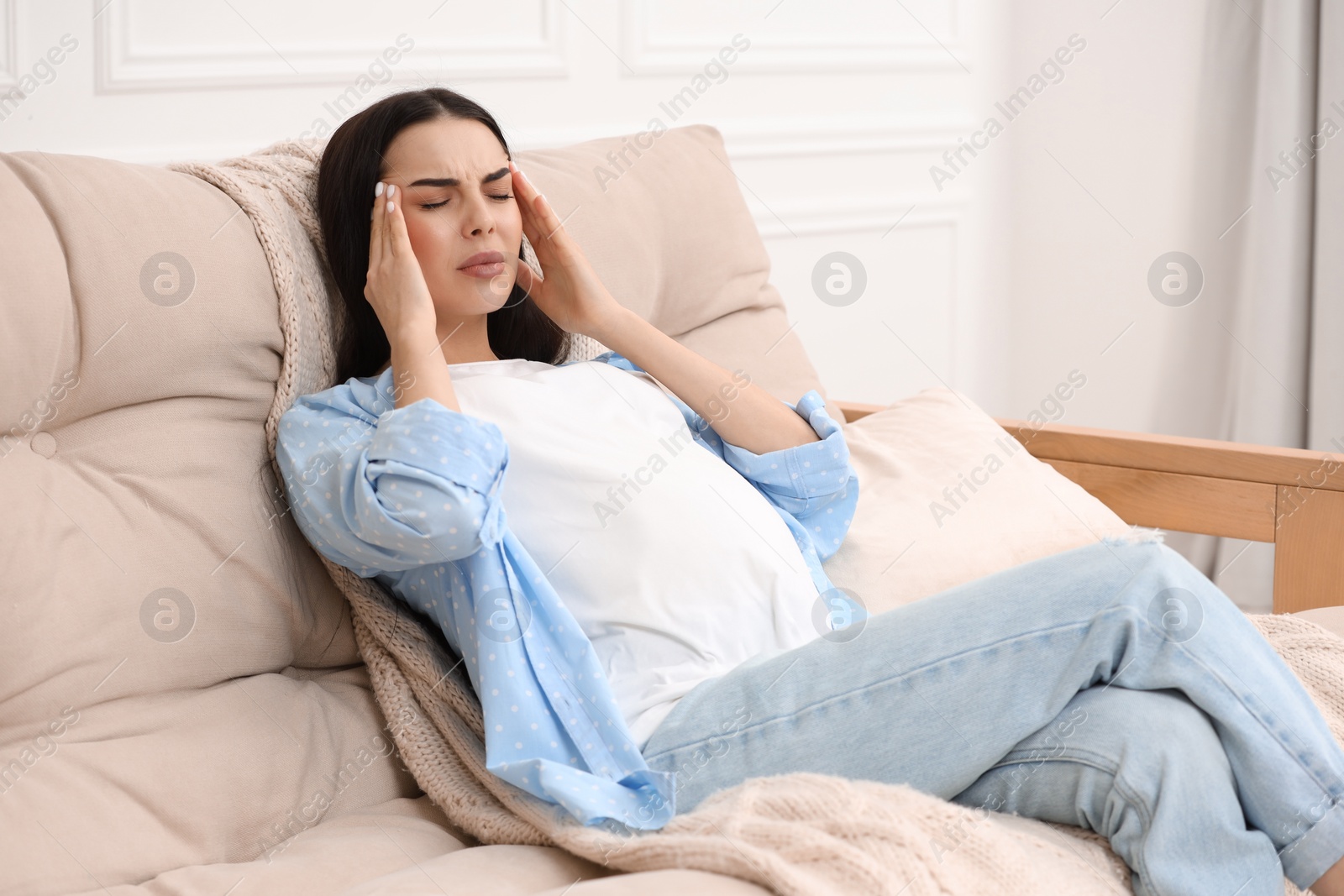 Photo of Pregnant woman suffering from headache on sofa at home