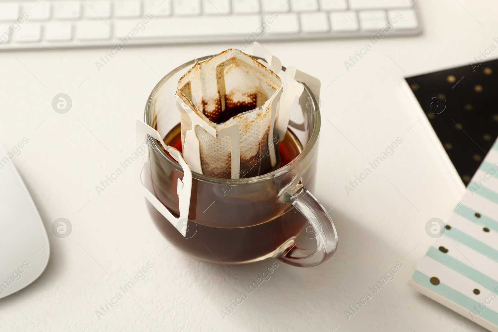 Photo of Glass cup with drip coffee bag on white table, closeup
