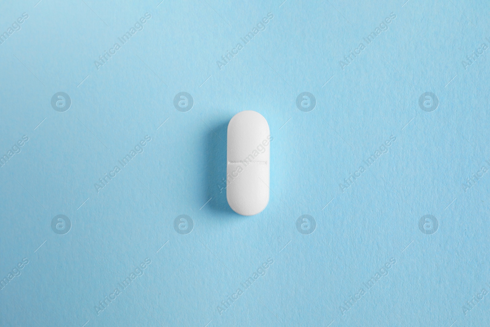 Photo of One white pill on light blue background, top view