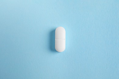 One white pill on light blue background, top view