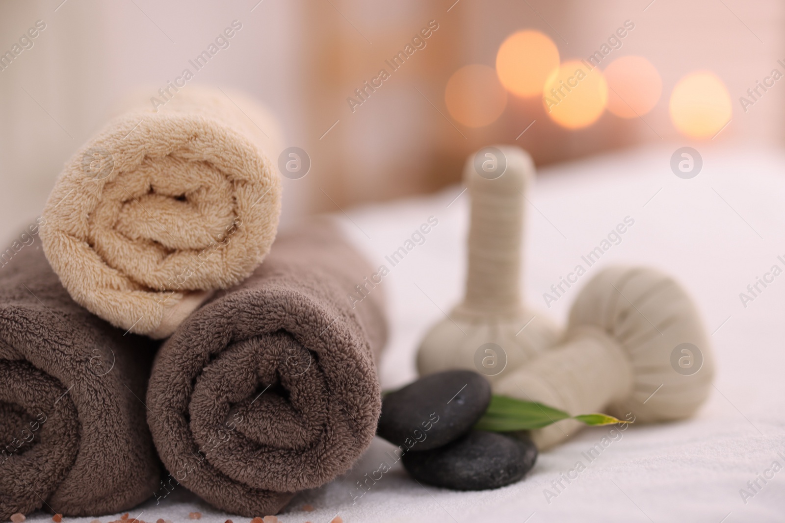 Photo of Spa stones, rolled towels and herbal bags on massage table indoors, closeup