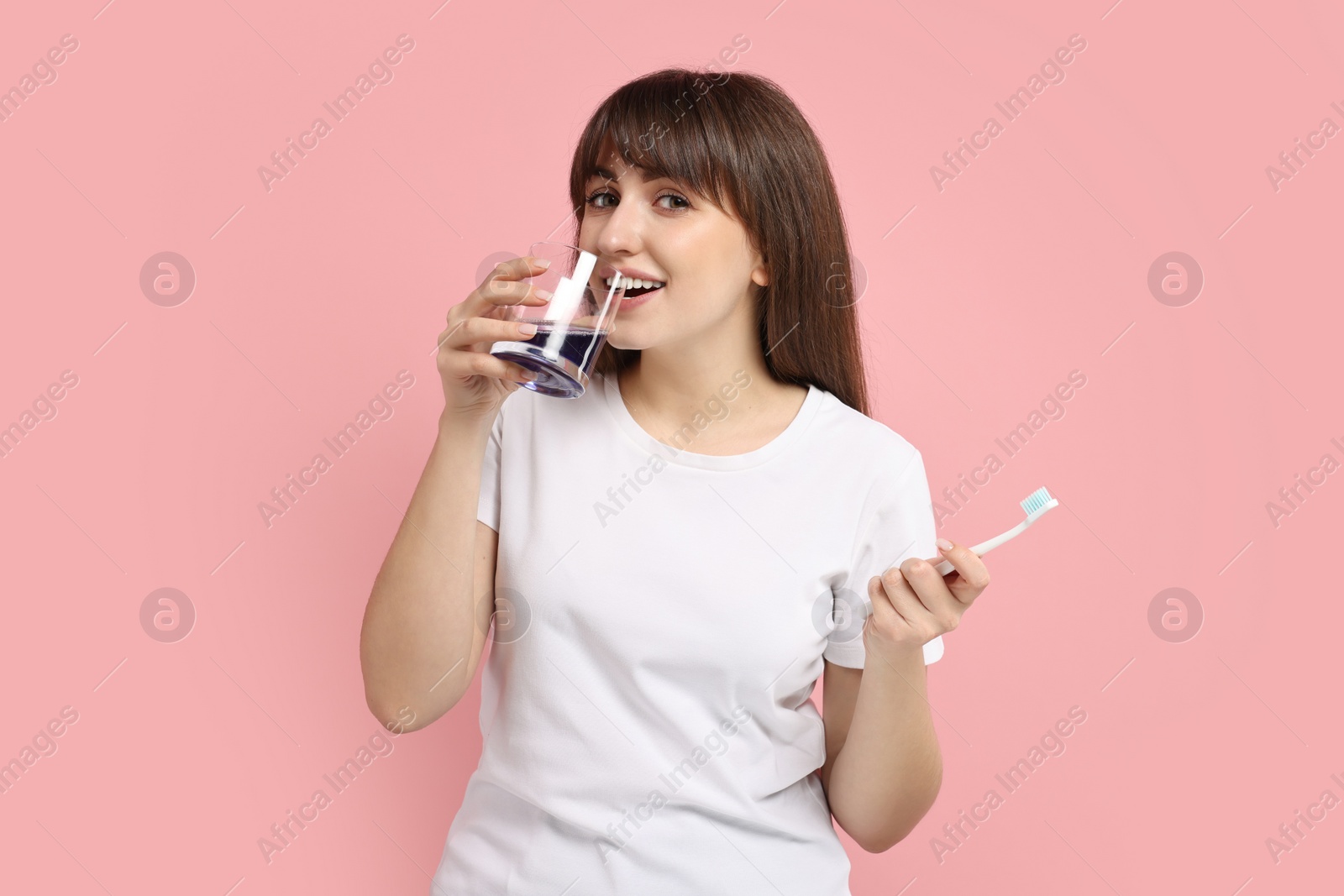 Photo of Young woman using mouthwash on pink background