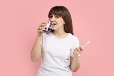 Young woman using mouthwash on pink background