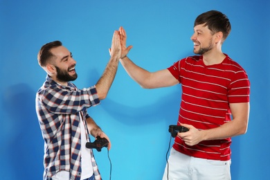 Emotional men playing video games with controllers on color background
