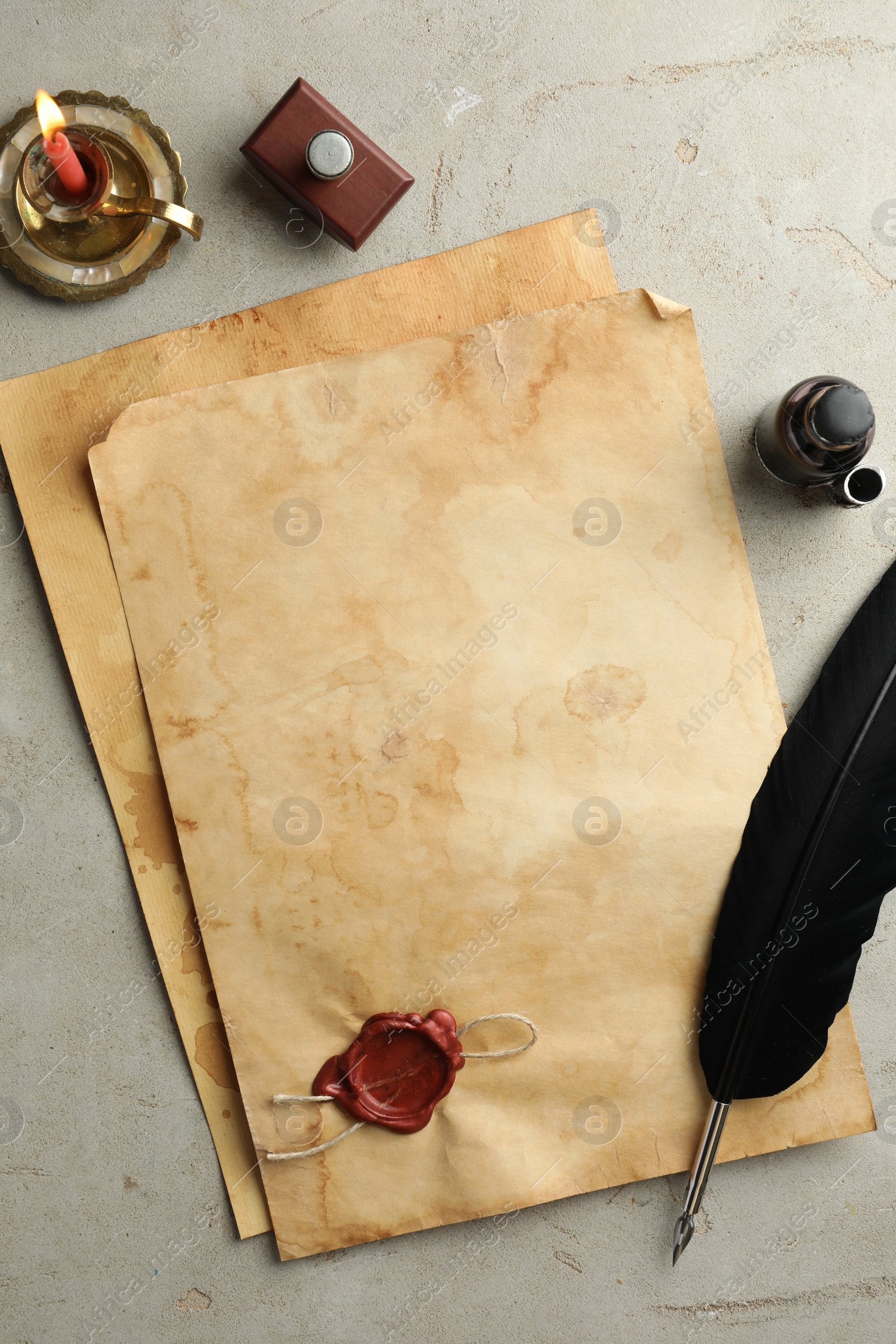 Photo of Sheet of old parchment paper with wax stamp, black feather, inkwell and candle on grey table, flat lay