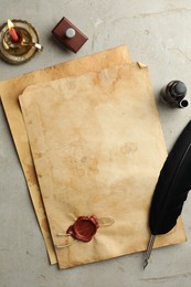 Sheet of old parchment paper with wax stamp, black feather, inkwell and candle on grey table, flat lay