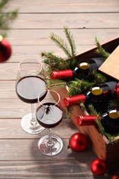 Wooden crate with bottles of wine, glasses, fir twigs and red Christmas balls on table