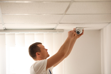 Photo of Technician installing CCTV camera on ceiling indoors