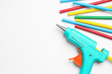 Turquoise glue gun and sticks on white background, flat lay. Space for text
