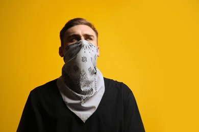 Photo of Young man with bandana covering his face on yellow background, low angle view