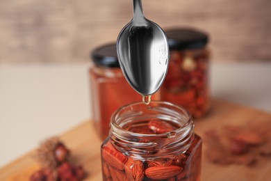 Photo of Honey dripping from spoon into glass jar with nuts, closeup