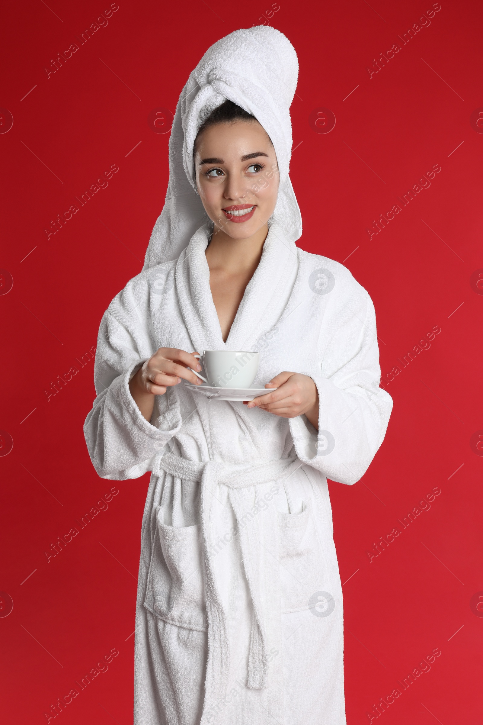 Photo of Young woman in bathrobe with cup of coffee on red background