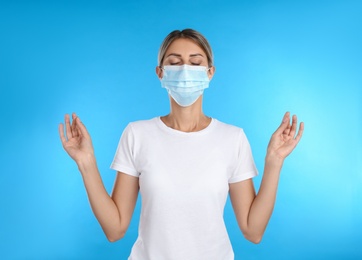 Photo of Woman in protective mask meditating on light blue background. Dealing with stress caused by COVID‑19 pandemic