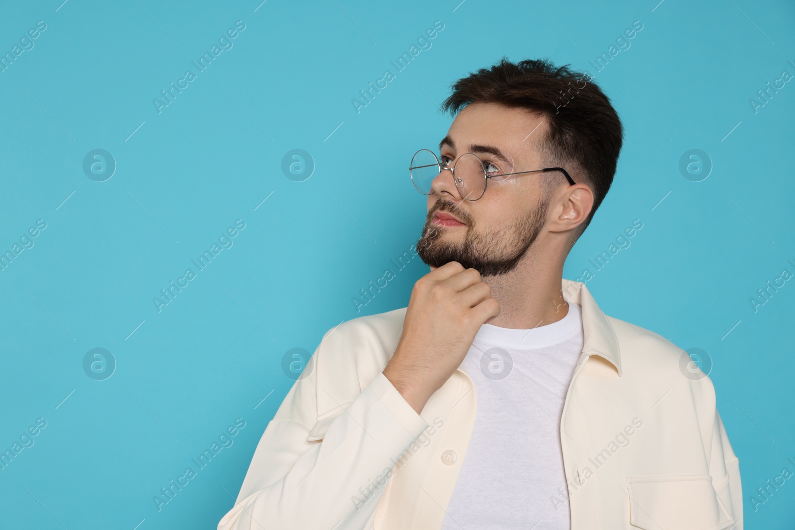 Photo of Thoughtful man in white jacket and eyeglasses on light blue background, space for text