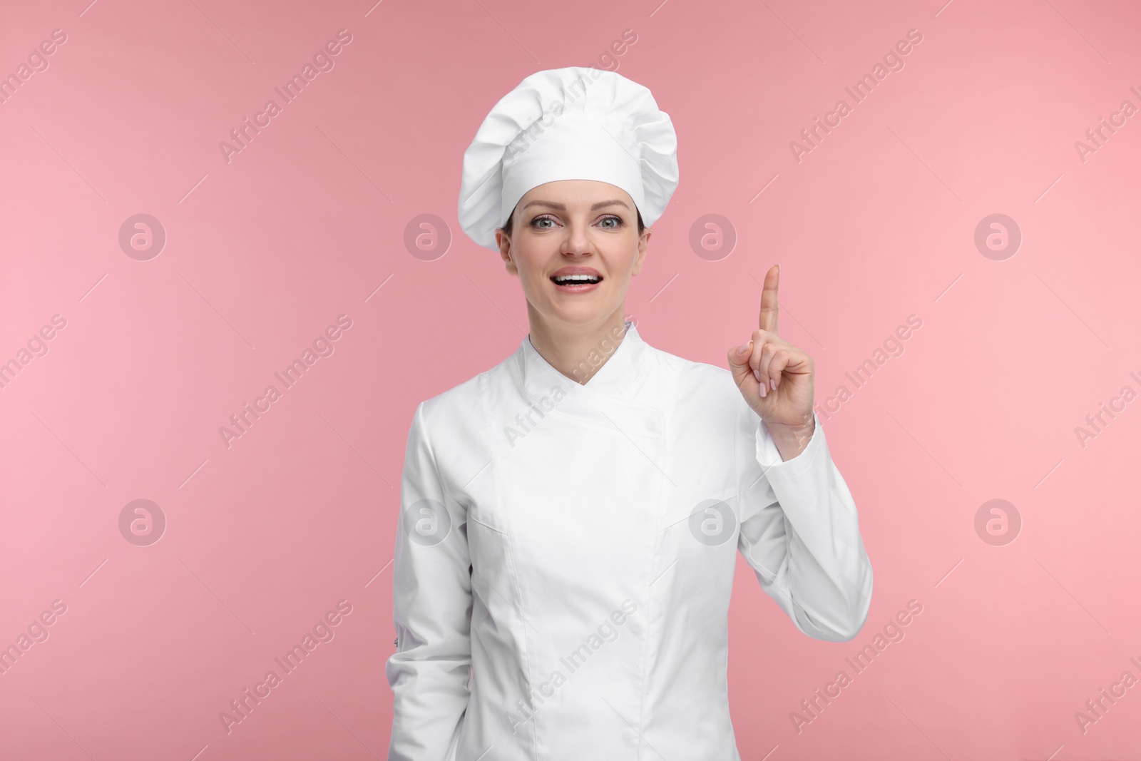 Photo of Happy chef in uniform pointing at something on pink background