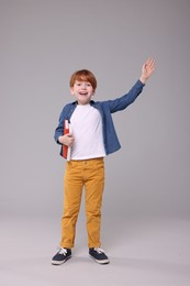 Photo of Happy schoolboy with books waving hello on grey background