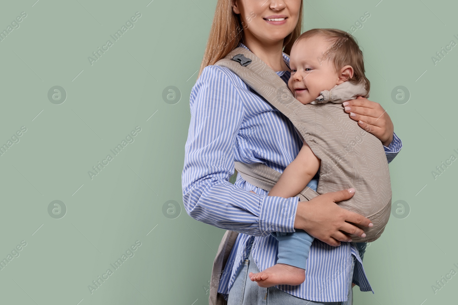 Photo of Mother holding her child in sling (baby carrier) on olive background, closeup. Space for text