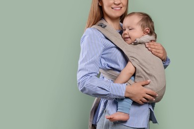 Mother holding her child in sling (baby carrier) on olive background, closeup. Space for text