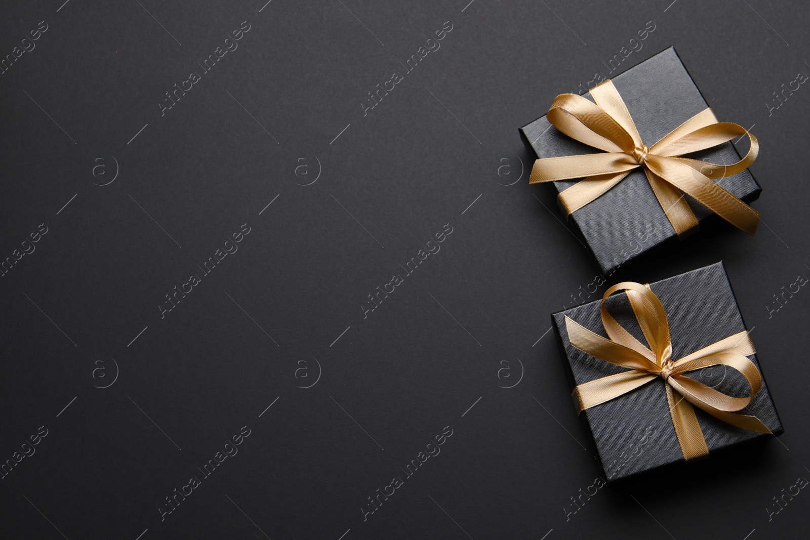 Photo of Shiny gift box with golden bow on black background, flat lay. Space for text